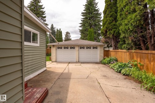 Detached two-car garage with panel garage doors featuring decorative window inserts, situated at the end of a concrete driveway - 7816 142 Street, Edmonton, AB 