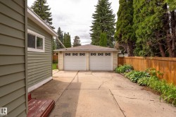 Detached two-car garage with panel garage doors featuring decorative window inserts, situated at the end of a concrete driveway - 