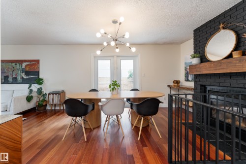 Spacious dining area featuring wood-finish flooring, a modern chandelier, double French doors, and a black brick fireplace with a wood mantel - 7816 142 Street, Edmonton, AB 