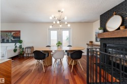 Spacious dining area featuring wood-finish flooring, a modern chandelier, double French doors, and a black brick fireplace with a wood mantel - 