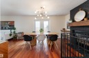 Spacious dining area featuring wood-finish flooring, a modern chandelier, double French doors, and a black brick fireplace with a wood mantel - 7816 142 Street, Edmonton, AB 