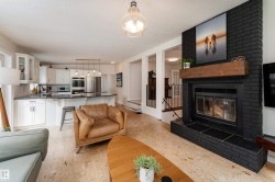 Open-concept living space featuring a black brick fireplace with a wood mantel, a kitchen island with seating, white cabinetry, and stainless steel appliances - 