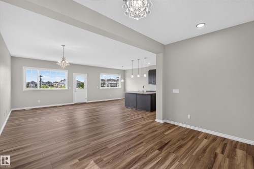 Spacious open-concept living area featuring wood-finish flooring, light gray wall tones, and white baseboards - 2460 15 Avenue, Edmonton, AB 