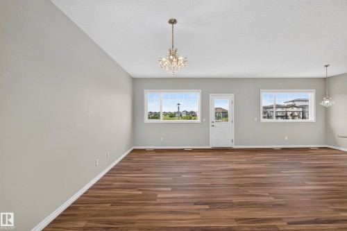 Expansive interior featuring wood-finish flooring, two large windows, a glass-paned door, and two crystal chandeliers - 2460 15 Avenue, Edmonton, AB 