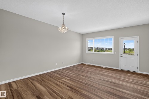 Spacious room featuring wood-finish flooring, a contemporary crystal chandelier, a large multi-pane window, and a white exterior door with an upper glass pane - 2460 15 Avenue Nw, Edmonton, AB - Indoor Photo Showing Other Room