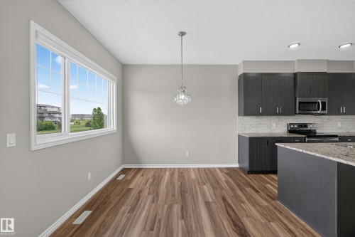 Open-concept dining area featuring wood-finish flooring, a contemporary chandelier, and a large window - 2460 15 Avenue, Edmonton, AB 