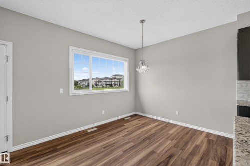 Spacious room featuring wood-finish flooring, light grey walls, and a large window - 2460 15 Avenue, Edmonton, AB 