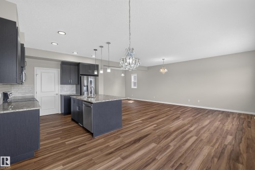 Open-concept living space featuring wood-finish flooring, a kitchen island with granite countertops, stainless steel appliances, and sleek dark cabinetry - 2460 15 Avenue, Edmonton, AB 