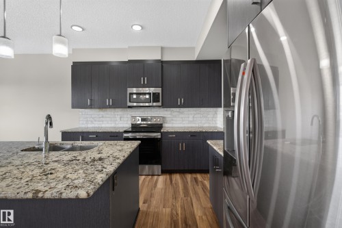 Kitchen featuring granite countertops, dark wood-finish cabinetry, stainless steel appliances, a subway tile backsplash, and wood-finish flooring - 2460 15 Avenue, Edmonton, AB 