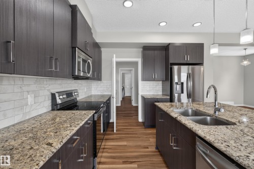Modern kitchen featuring dark wood-finish cabinetry, light granite countertops, stainless steel appliances, and a white subway tile backsplash - 2460 15 Avenue, Edmonton, AB 