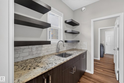 Utility room featuring a stainless steel sink, patterned countertop, subway tile backsplash, dark wood-finish cabinetry, and wood-finish flooring - 2460 15 Avenue, Edmonton, AB 
