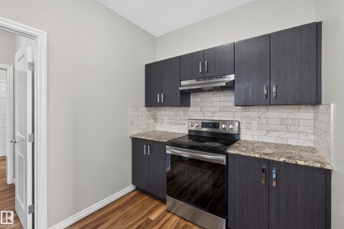 Kitchen area featuring dark wood-grain cabinetry, stainless steel range with matching range hood, and a subway tile backsplash - 2460 15 Avenue, Edmonton, AB 