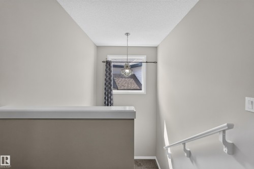Upper-level landing featuring neutral paint, a contemporary pendant light fixture, and a window with natural light - 2460 15 Avenue, Edmonton, AB 