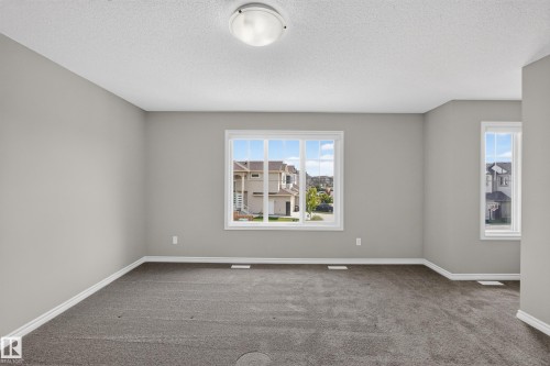 Carpeted room featuring light gray walls, white trim, and a prominent window - 2460 15 Avenue, Edmonton, AB 