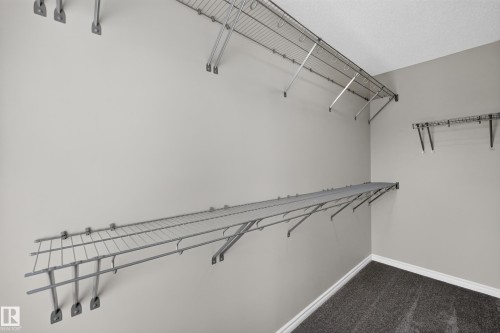Walk-in closet featuring wire shelving, wire hanging rods, light gray wall paint, and gray carpet flooring with white baseboards - 2460 15 Avenue, Edmonton, AB 