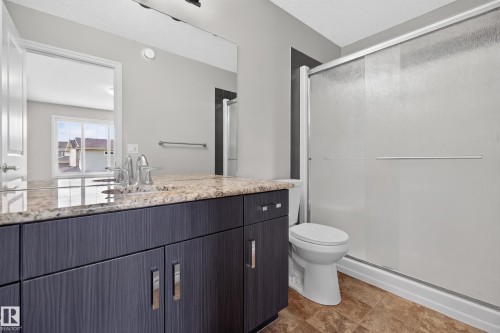 Bathroom featuring a dark wood-finish vanity with a light-toned countertop, a large wall-mounted mirror, a commode, and a shower enclosure with sliding glass doors - 2460 15 Avenue, Edmonton, AB 