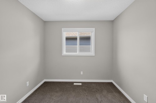 Neutral gray walls with white trim, dark gray carpet, a single window with white blinds, and a white ceiling with a textured finish - 2460 15 Avenue, Edmonton, AB 