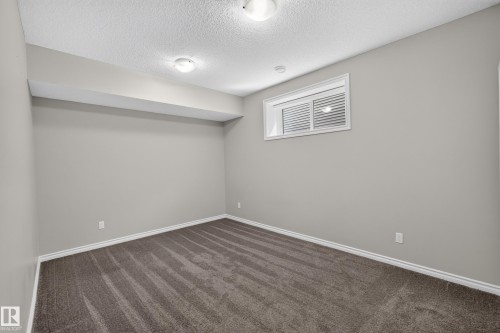 Carpeted room featuring light gray walls, a textured ceiling, a rectangular window with blinds, and white baseboards - 2460 15 Avenue, Edmonton, AB 