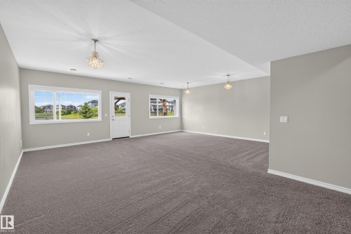 Spacious open-concept room featuring plush carpeting, light gray wall tones, and multiple large windows for abundant natural light - 2460 15 Avenue, Edmonton, AB 