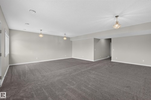 Spacious room featuring gray wall paint, gray carpeting, recessed ceiling lighting, and three chandelier-style light fixtures - 2460 15 Avenue, Edmonton, AB 