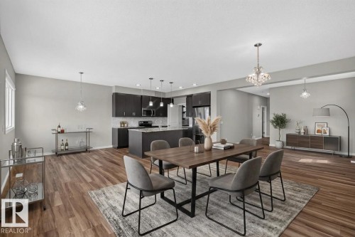 Open-concept living space featuring wood-finish flooring, a modern kitchen with dark cabinetry, stainless steel appliances, and a central island - 2460 15 Avenue, Edmonton, AB 