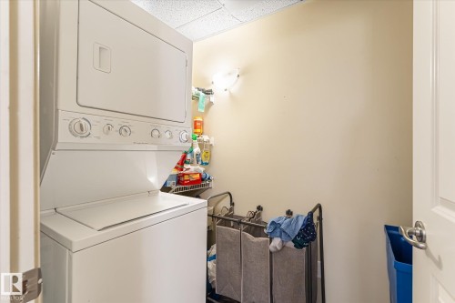 Dedicated laundry area featuring a white stacked washer and dryer, a recessed shelf, and a wall-mounted light fixture - 402 10121 80 Avenue, Edmonton, AB 