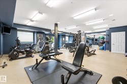 Fitness center featuring a textured flooring surface, multiple windows, recessed lighting, wall-mounted television, and a paneled white door - 