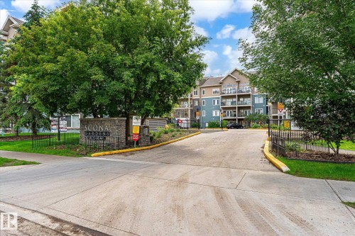 Scona Gardens entrance featuring a stone monument with wrought iron fencing, surrounded by mature trees and manicured landscaping, with a multi-story residential building in the background - 402 10121 80 Avenue, Edmonton, AB 