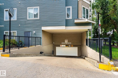 Underground parking entrance featuring a white garage door, concrete ramp, and black metal railings - 402 10121 80 Avenue, Edmonton, AB 