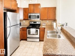 Kitchen featuring warm wood cabinetry, stainless steel appliances, a double basin sink, speckled countertops, and a tiled backsplash - 