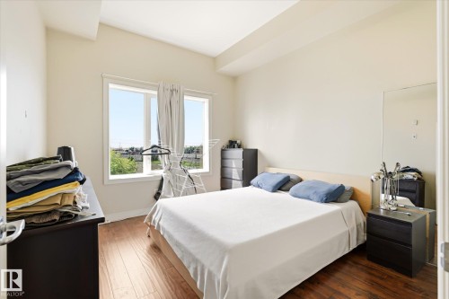 Bedroom featuring wood-finish flooring, a double window with a light-colored frame, cream-painted walls, and a light-colored ceiling - 402 10121 80 Avenue, Edmonton, AB 
