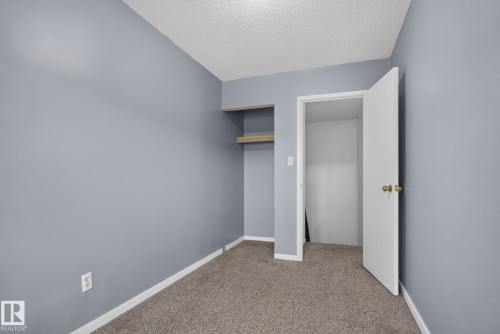 Neutral gray walls with textured ceiling and a built-in closet featuring two natural wood shelves - 401 2908 116A Avenue, Edmonton, AB 