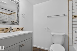 Bathroom featuring a single vanity with a white countertop and gray cabinetry, a decorative framed mirror, and a white toilet - 