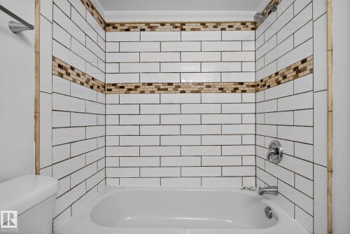 Bathtub with white subway tile surround, featuring two decorative mosaic tile accent bands - 401 2908 116A Avenue, Edmonton, AB 