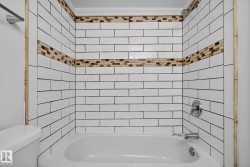 Bathtub with white subway tile surround, featuring two decorative mosaic tile accent bands - 