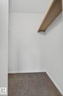 Walk-in closet with overhead shelving, neutral carpeting, and white baseboards - 