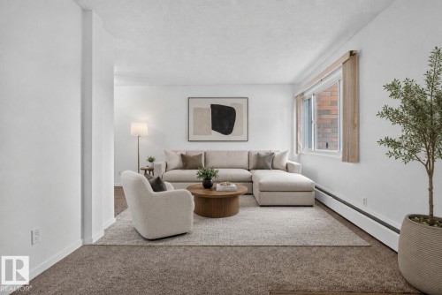 Spacious living area featuring neutral carpeting, white walls, a large window with vertical blinds, and baseboard heating - 401 2908 116A Avenue, Edmonton, AB 
