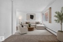 Spacious living area featuring neutral carpeting, white walls, a large window with vertical blinds, and baseboard heating - 401 2908 116A Avenue, Edmonton, AB 