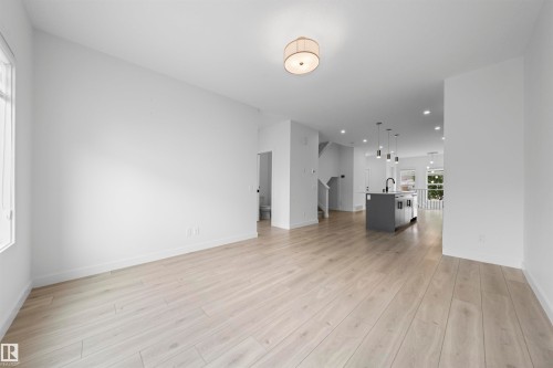 Open-concept interior featuring light wood-finish flooring, white walls, and a contemporary semi-flush ceiling light - 2953 Coughlan Green Green, Edmonton, AB 
