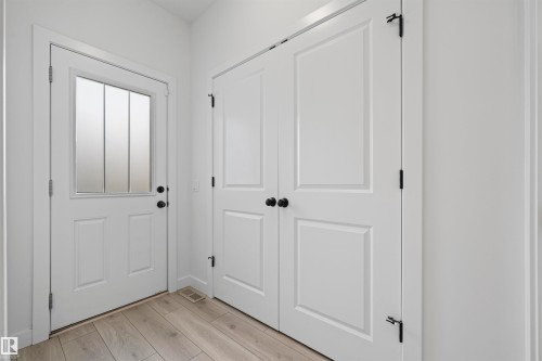 Entryway featuring a white paneled door with frosted glass insert, black hardware, wood-finish flooring, and white bifold closet doors - 2953 Coughlan Green Green, Edmonton, AB 