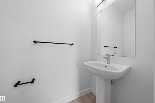 Pedestal sink with chrome faucet, large frameless mirror, and black wall-mounted towel bars - 2953 Coughlan Green Green, Edmonton, AB 