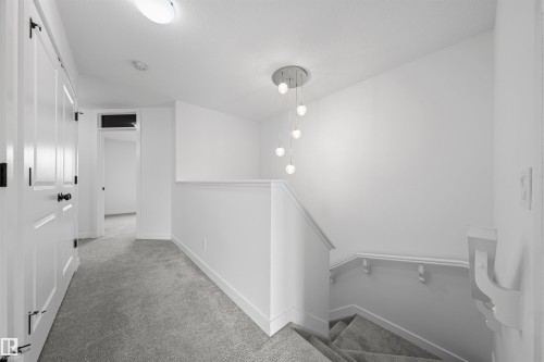 Upper-level hallway featuring plush gray carpeting, white trim, and a contemporary chandelier - 2953 Coughlan Green Green, Edmonton, AB 