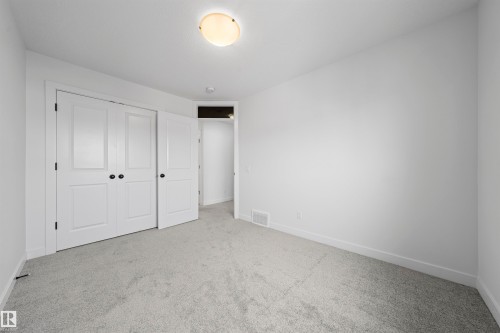 Carpeted room featuring a double bifold closet with black hardware, white walls, white trim, and a ceiling-mounted light fixture - 2953 Coughlan Green Green, Edmonton, AB 