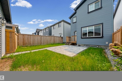 Rear exterior featuring blue horizontal siding, black trim windows, a ground-level patio, and a wooden fence - 2953 Coughlan Green Green, Edmonton, AB 