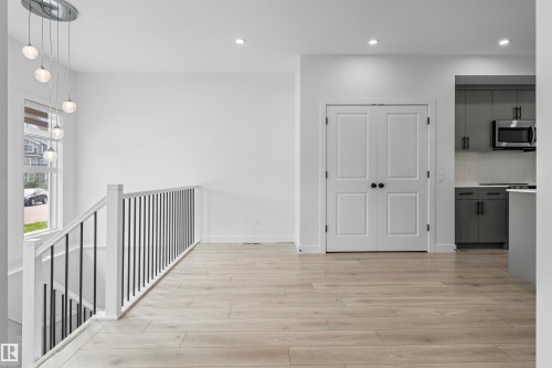 Open concept area featuring wood-finish flooring, a contemporary chandelier, white walls, and a staircase with a white banister and black spindles - 2953 Coughlan Green Green, Edmonton, AB 