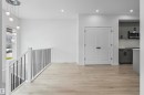 Open concept area featuring wood-finish flooring, a contemporary chandelier, white walls, and a staircase with a white banister and black spindles - 2953 Coughlan Green Green, Edmonton, AB 