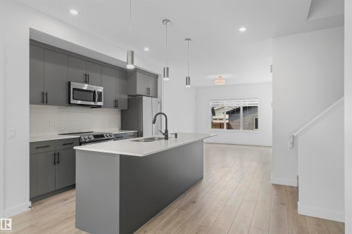 Kitchen featuring an island with a sink and pendant lighting, stainless steel appliances, grey cabinetry, and wood-finish flooring - 2953 Coughlan Green Green, Edmonton, AB 