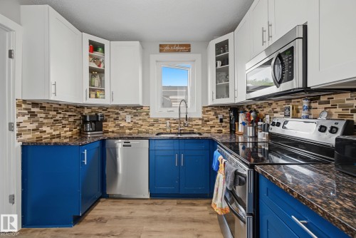 Contemporary kitchen featuring two-tone cabinetry, stainless steel appliances, granite countertops, and a mosaic tile backsplash - 3622 115 Avenue, Edmonton, AB 