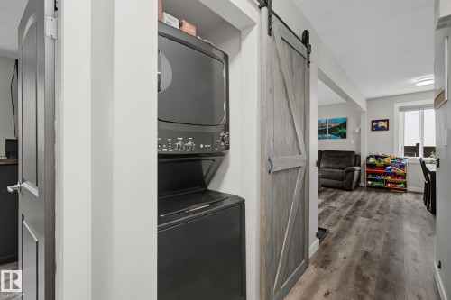 Compact laundry area featuring a stacked washer and dryer, wood-finish flooring, and a sliding barn door - 3622 115 Avenue, Edmonton, AB 