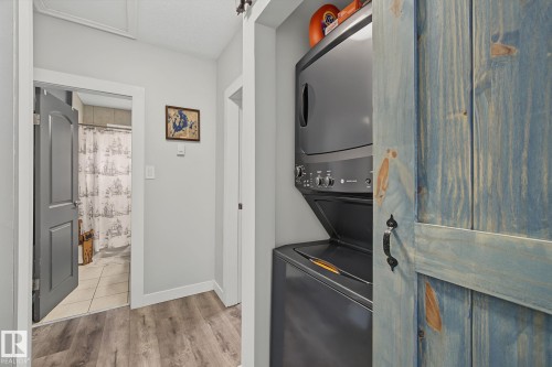Compact laundry area featuring a stacked washer and dryer, wood-finish flooring, and a rustic blue wood barn door - 3622 115 Avenue, Edmonton, AB 